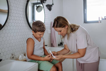 Mutter, die den Blutzuckerspiegel ihres Sohnes zu Hause mit einem Blutzuckermessgerät mit Fingerspitze kontrolliert. Der zuckerkranke Junge mit Blut an der Fingerspitze, der auf die Analyse seines aktuellen Blutzuckerspiegels wartet. - HPIF32905