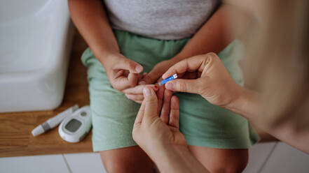 Mutter, die den Blutzuckerspiegel ihres Sohnes zu Hause mit einem Blutzuckermessgerät mit Fingerspitze kontrolliert. Der zuckerkranke Junge wartet auf die Ergebnisse seiner Blutuntersuchung. Mutter, die die Wange ihres Sohnes streichelt. - HPIF32911