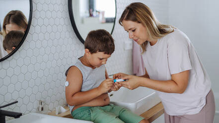 Mutter eines zuckerkranken Jungen, der sich Insulin in den Bauch spritzt. Ein kleiner Junge mit Typ-1-Diabetes nimmt Insulin mit einer Spritze im Badezimmer ein. - HPIF32915