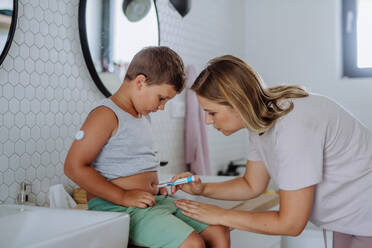 Mutter eines zuckerkranken Jungen, der sich Insulin in den Bauch spritzt. Ein Junge mit Typ-1-Diabetes nimmt Insulin mit einer Spritzennadel im Badezimmer ein. - HPIF32917
