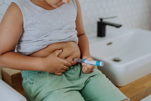 Kleiner Junge mit Diabetes, der sich Insulin in den Bauch spritzt. Nahaufnahme eines kleinen Jungen mit Typ-1-Diabetes, der mit einer Spritze Insulin einnimmt. - HPIF32918