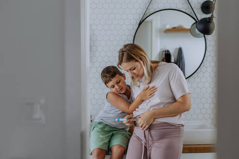 Woman injecting insulin in her belly, while her son watching and supporting her. Close up of mother with with type 1 diabetes taking insuling with syringe needle. - HPIF32921