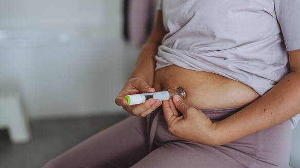 Woman injecting insulin with insulin pen in her abdomen in bathroom. Close up of mother with type 1 diabetes taking insuling with syringe needle. - HPIF32924