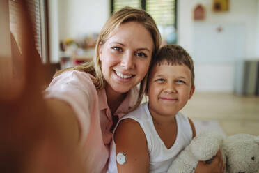 Selfie portrait of mother and diabetic boy with a continuous glucose monitor on his arm. The CGM device makes the life of the schoolboy easier, helping manage his illness and focus on other activities. - HPIF32932