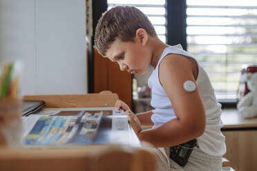 The diabetic boy doing homework, while wearing a continuous glucose monitoring sensor on his arm. CGM device making life of school boy easier, helping manage his illness and focus on other activities. - HPIF32936