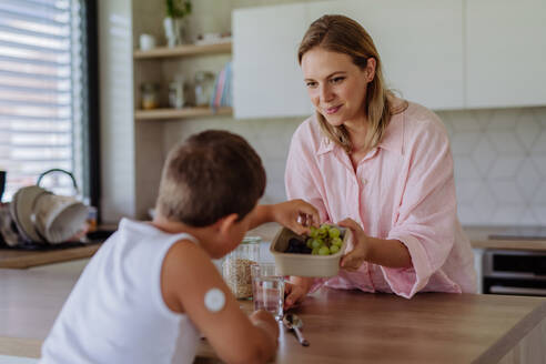 Diabetic boy with a continuous glucose monitor is careful with his diet. Mother checking what her son with diabetes eating. CGM device making life of school boy easier, helping manage his illness and focus on other activities. - HPIF32939