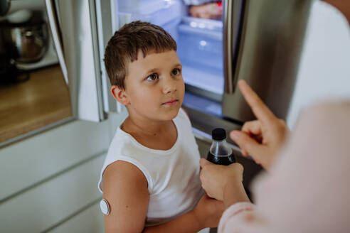 Diabetic boy with a continuous glucose monitor can't drink sweetened soda, sugar drink. Mother checking what her son with diabetes drinking. - HPIF32943