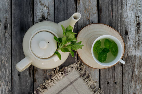 Top view of a teapot and tea cup with homemade lemon balm tea on a wooden table. Homegrown herbs are used to prepare herbal tea. Lemon balm as a medicinal herb. - HPIF32944