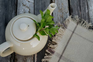 Top view of a teapot with homemade lemon balm tea on a wooden table. Homegrown herbs are used to prepare herbal tea. Lemon balm as a medicinal herb. - HPIF32945