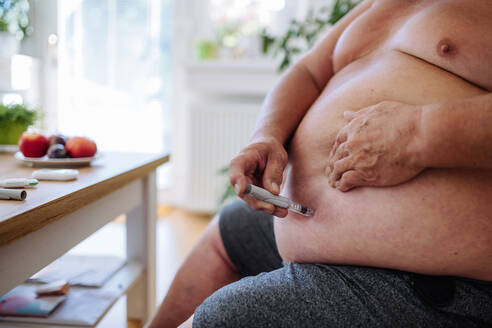 Overweight man with diabetes injecting insulin in his abdomen. Close up of man with type 1 diabetes taking insuling with insuling pen. - HPIF32957