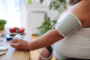 Overweight man measuring his blood pressure at home. Man with high blood pressure using at-home blood pressure monitor. - HPIF32969