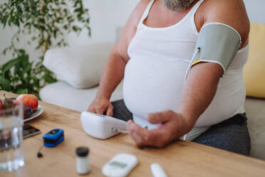 Overweight man measuring his blood pressure at home. Man with high blood pressure using at-home blood pressure monitor. - HPIF32970