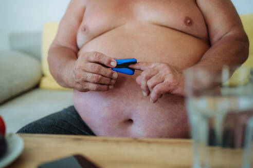 Ein übergewichtiger Mann verwendet zu Hause ein Pulsoximeter, um die Sauerstoffsättigung des Blutes zu messen. - HPIF32972