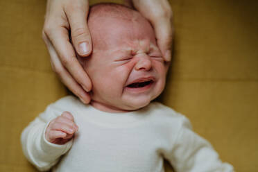 Close-up of parent stroking his crying baby lying in a bed. - HPIF33066