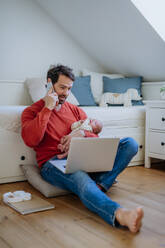 Father holding his newborn crying baby during working on a laptop. - HPIF33080
