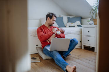 Father holding his newborn crying baby during working on a laptop. - HPIF33081