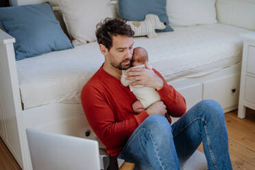 Father holding his newborn crying baby during working on a laptop. - HPIF33092