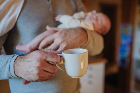 Close- up of father holding her newborn baby and a cup of coffee. - HPIF33124