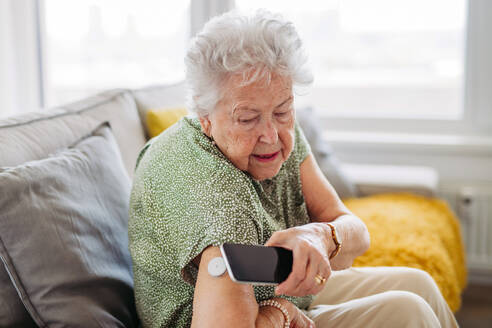 Diabetic senior patient checking blood glucose level at home using continuous glucose monitor. Elderly woman connecting her CGM with smarphone to see her blood sugar levels in real time. - HPIF33158