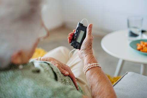Close up of diabetic senior patient checking her blood sugar level on insulin pump. Portrait of senior woman with type 1 diabetes taking insuling from tethered insulin pump. - HPIF33174