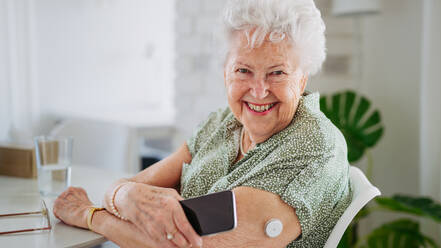 Diabetic senior patient checking blood glucose level at home using continuous glucose monitor. Elderly woman connecting her CGM with smarphone to see her blood sugar levels in real time. Banner with copy space. - HPIF33191