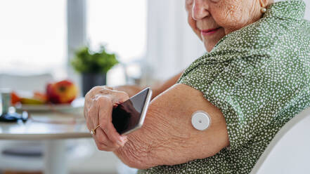 Diabetic senior patient checking blood glucose level at home using continuous glucose monitor. Elderly woman connecting her CGM with smarphone to see her blood sugar levels in real time. - HPIF33193