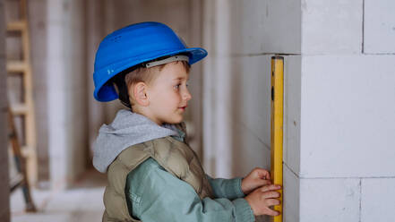 Little boy in unfinished house measuring wall in unfinished house with a spirit level. - HPIF33205