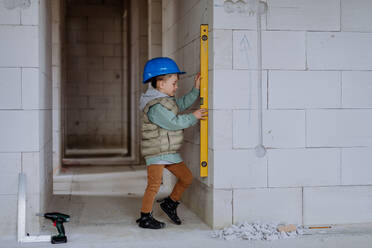 Little boy in unfinished house measuring wall in unfinished house with a spirit level. - HPIF33206