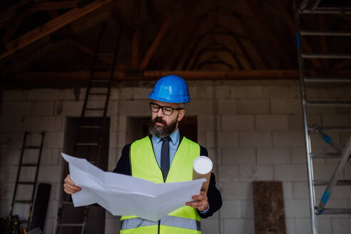 Mature businessman controlling blueprints from an unfinished house. - HPIF33298