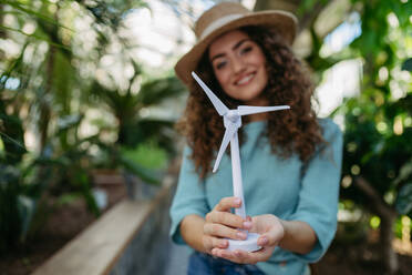 Junge Frau in einem botanischen Garten mit einem Modell einer Windturbine, Konzept der grünen Energie. - HPIF33318