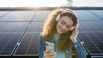 Portrait of young excited woman, owner on roof with solar panels, listening music. - HPIF33351