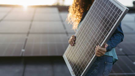 Close up of a woman holding solar panel on the roof with photovoltaics panels. - HPIF33360