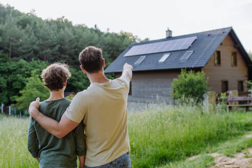 Father showing a roof with solar panels to his son. Alternative energy, saving resources and sustainable lifestyle concept. - HPIF33365