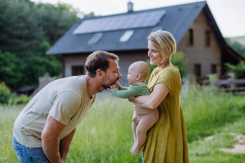 Happy family near their house with a solar panels. Alternative energy, saving resources and sustainable lifestyle concept. - HPIF33371