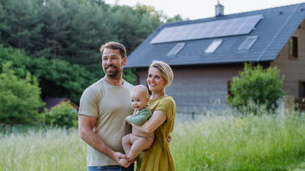 Happy family near their house with a solar panels. Alternative energy, saving resources and sustainable lifestyle concept. - HPIF33372