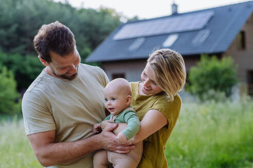 Happy family near their house with a solar panels. Alternative energy, saving resources and sustainable lifestyle concept. - HPIF33373