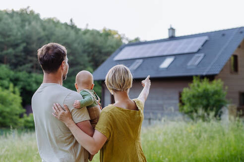 Rear view of family near their house with a solar panels. Alternative energy, saving resources and sustainable lifestyle concept. - HPIF33376