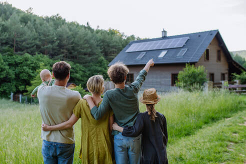 Rear view of family near their house with a solar panels. Alternative energy, saving resources and sustainable lifestyle concept. - HPIF33380