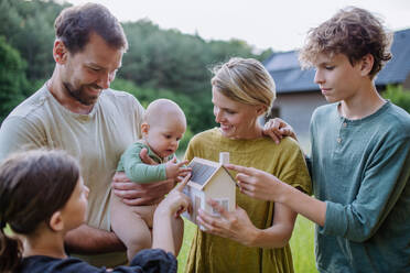 Happy family with three children holding a model of house ith solar photovoltaics. Alternative energy, saving resources and sustainable lifestyle concept. - HPIF33381