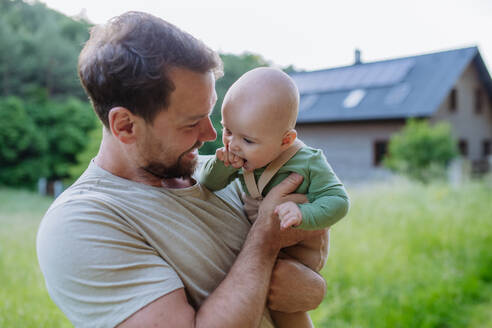 Happy father with baby boy standing in front of their house with solar panels. - HPIF33386