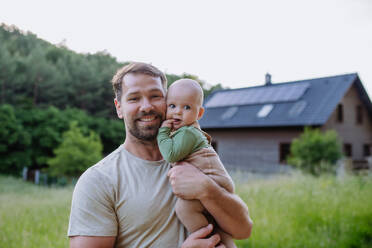 Happy father with baby boy standing in front of their house with solar panels. - HPIF33387