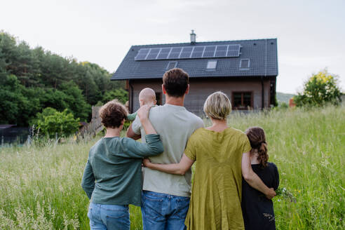 Rear view of family near their house with a solar panels. Alternative energy, saving resources and sustainable lifestyle concept. - HPIF33390