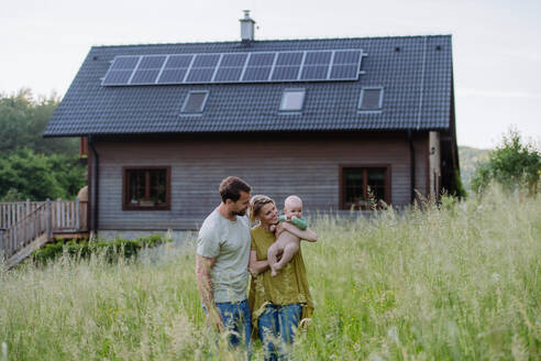 Happy family with baby near their house with a solar panels. Alternative energy, saving resources and sustainable lifestyle concept. - HPIF33397