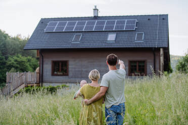 Rear view of family near their house with a solar panels. Alternative energy, saving resources and sustainable lifestyle concept. - HPIF33398