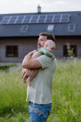 Happy father with baby boy standing in front of their house with solar panels. - HPIF33399