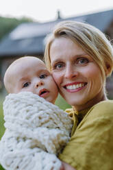 Portrait of a happy mother with her small baby, standing in front of their house. - HPIF33403