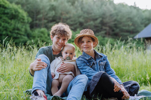 Portrait of three children, siblings sitting in a grass, having fun together. - HPIF33404