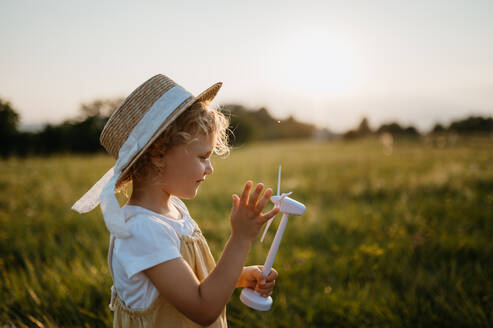 Little girl with model of wind turbine, standing in the middle of meadow Concept of renewable resources. Importance of alternative energy sources and long-term sustainability for future generations - HPIF33408