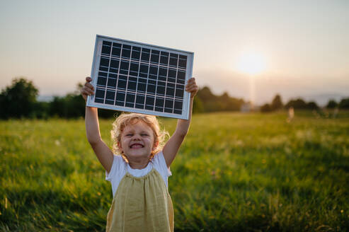 Little girl with model of solar panel, standing in the middle of meadow Concept of renewable resources. Importance of alternative energy sources and long-term sustainability for future generations - HPIF33409