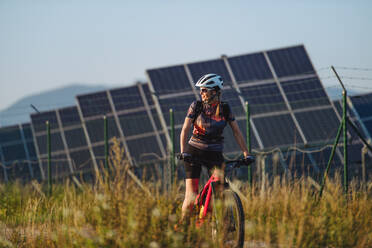 Schöner Radfahrer, der während einer sommerlichen Radtour in der Natur vor den Solarmodulen eines Solarparks fährt. Ein Solarpark als Lösung für eine nachhaltigere Energiezukunft. - HPIF33448